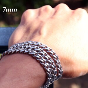 K&ouml;nnte beinhalten: Ein silbernes Kettenarmband mit einer Breite von 7 mm. Das Armband ist an einem Handgelenk &uuml;bereinander gelegt.