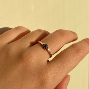 May include: A silver ring featuring a black evil eye charm. The ring is worn on a person's finger.