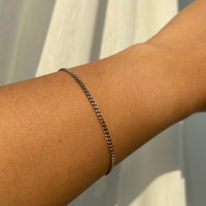 May include: A silver curb chain bracelet. The bracelet is made of small, interlocking links and is worn on the arm. The bracelet is a simple, elegant piece of jewellery.