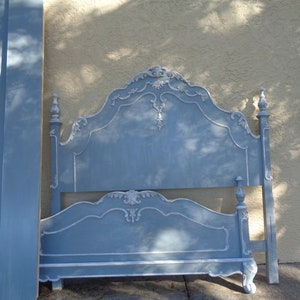 May include: A light blue bed frame with ornate detailing. The headboard and footboard feature decorative carvings and a distressed finish. The bed frame is painted in a soft blue with white accents, showcasing a vintage aesthetic.
