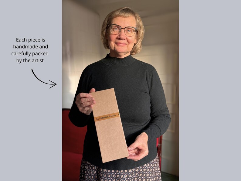 Professional textile artist Elina Lūsis-Grīnberga holding a carefully packaged handmade artwork, labeled “ELG | Handmade in Latvia” – each piece is individually crafted and packed with care.