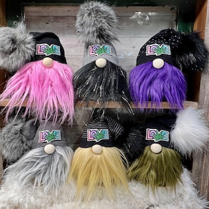 May include: A collection of eight gnomes with different colored beards and hats. Each gnome has a black and white patch on their hat that says "LOVE" with a marijuana leaf design.