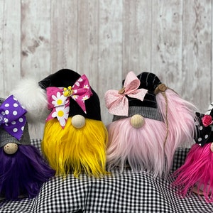 May include: Four gnomes with different colored hair and bows. The gnomes are wearing black and gray hats with different colored bows. The gnomes are sitting on a black and white checkered surface.