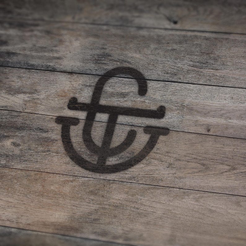May include: A dark, stylized monogram logo is cast as a shadow on a weathered, wooden surface. The logo features a stylized "f" intertwined with a "t" and a curved element, creating a unique design. The wood grain adds texture.