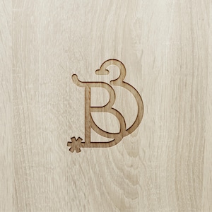 May include: A wooden monogram featuring the letter "B" with a decorative flourish and a star-like element. The design is carved into a light-colored wood surface, creating a subtle contrast in tones.