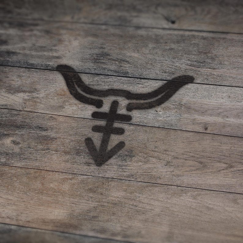May include: A dark brown graphic of a bull's head with a stylized symbol below it, stenciled on a wooden surface. The wood grain is visible, with a mix of light and dark brown tones.