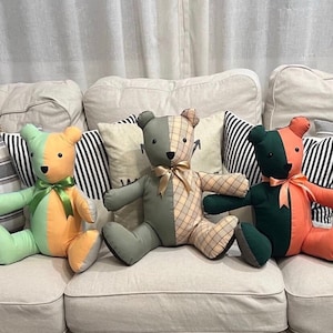May include: Four patchwork teddy bears sitting on a light beige sofa. The bears are made of different fabrics, including green, orange, and plaid. The bears are all wearing bows around their necks.