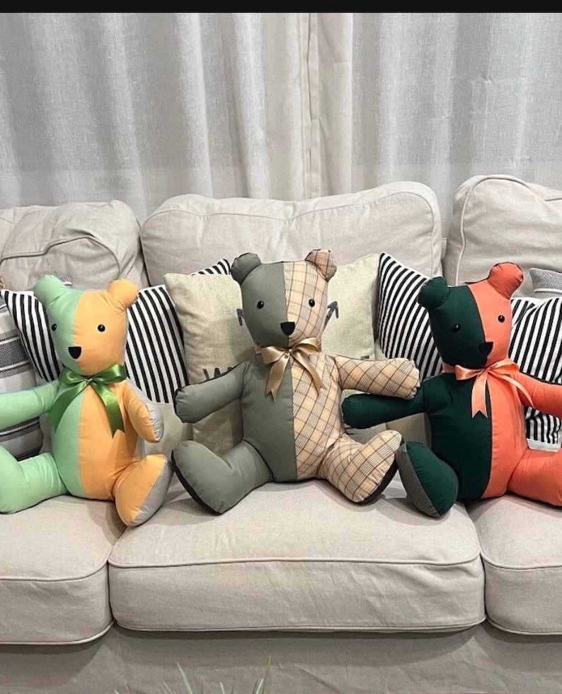 May include: Four patchwork teddy bears sitting on a light beige sofa. The bears are made of different fabrics, including green, orange, and plaid. The bears are all wearing bows around their necks.