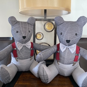 May include: Two gray teddy bears wearing gray pants, white shirts, and red suspenders. Both bears are wearing a light blue bow tie.