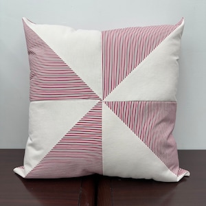 May include: A square throw pillow with a white background and red and white striped fabric panels. The panels are arranged in a pinwheel pattern.