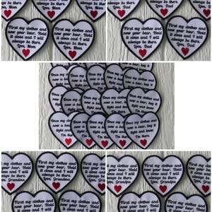 May include: A collection of white felt heart-shaped patches with black embroidered text. The text reads "First my clothes and now your bear. Hold it close and I will always be there. Love, Mom/Dad/Grandma/Grandpa". Each patch has a red heart in the centre.
