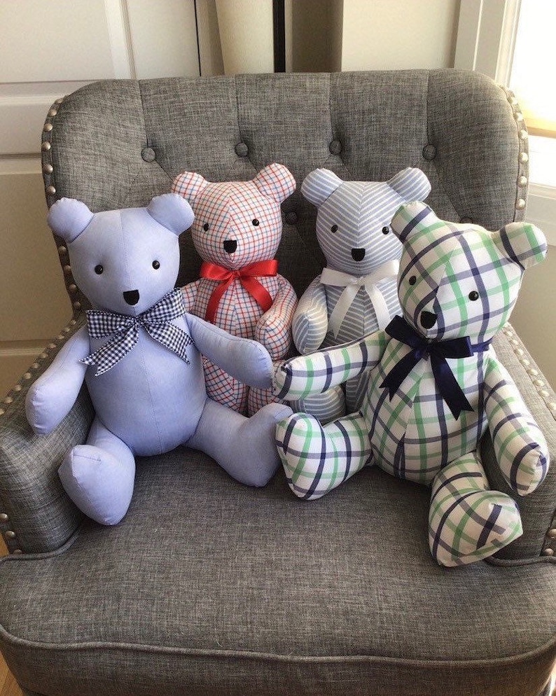 May include: Four plush teddy bears sitting on a grey sofa. The bears are made from different patterned fabrics, including blue and white stripes, red and white plaid, and green and blue plaid. Each bear has a bow tied around its neck.