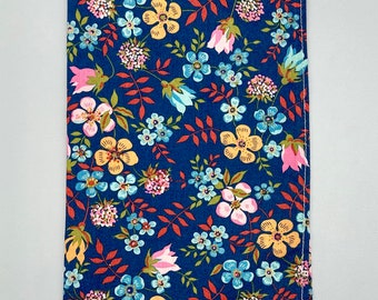May include: A blue fabric with a floral pattern. The fabric features pink, yellow, and green flowers on a dark blue background.