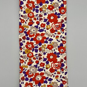 May include: A white fabric with a floral pattern in shades of orange, purple, and brown. The fabric has a subtle texture and a slightly distressed look.