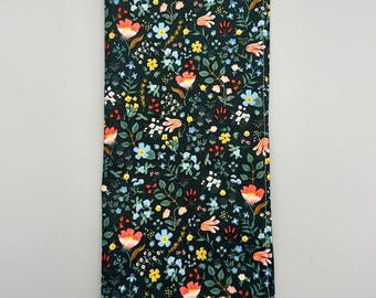 May include: A black fabric with a floral pattern in shades of red, orange, yellow, blue, and green. The fabric has a white border.