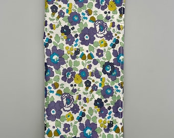 May include: A white fabric rectangle with a floral pattern in shades of purple, blue, and yellow. The fabric has a subtle sheen and a slightly textured surface.