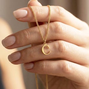 May include: A gold-toned necklace featuring a delicate curb chain and a single pendant in the shape of the capital letter C. The pendant is suspended from a small jump ring, and the entire piece exhibits a polished, metallic finish throughout.