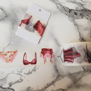 Könnte beinhalten: Eine Rolle Washi-Tape mit einem sich wiederholenden Muster aus Dessous, darunter ein BH, Höschen und ein Strumpfband. Das Band ist weiß mit roten und rosa Akzenten.