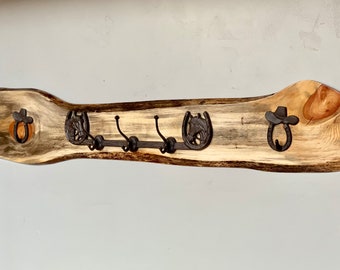 May include: A rustic wooden coat rack with three metal hooks. The rack is shaped like a branch and has a natural wood finish. The hooks are decorated with horseshoe and cowboy hat designs.