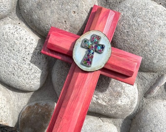 May include: A wooden cross with a red stain finish. The cross is decorated with a round, white wood slice with a silver cross adorned with colorful jewels.