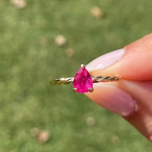 May include: A gold ring with a twisted band and a pear-shaped pink gemstone.