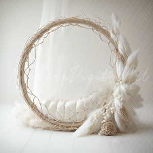 May include: A white, round, woven nest with a white, quilted cushion inside. The nest is decorated with white feathers and dried pampas grass.