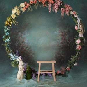 Peut inclure: Une figurine de lapin blanc est posée sur un tissu de tulle bleu clair devant un tabouret en bois. Une couronne florale composée de fleurs roses, blanches et violettes est suspendue sur un fond vert sarcelle.
