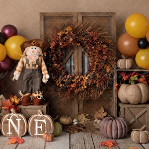 May include: A rustic autumn-themed first birthday party backdrop with a scarecrow, pumpkins, and balloons. The backdrop features a wooden door with an autumnal wreath, a wooden crate with pumpkins, and a wooden sign that says "ONE".