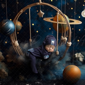 May include: A newborn baby wearing a blue and white checked sleepsuit and a blue knitted hat sleeps in a woven hoop decorated with planets and stars. The background is a dark blue with gold glitter.