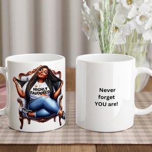 Op de afbeelding: Twee witte keramische mokken. Eén mok heeft een cartoonillustratie van een vrouw met lang bruin haar die op een stoel zit. De tekst "HIGHLY FAVOURED" staat op haar shirt. De andere mok heeft de tekst "Never forget YOU are!" erop gedrukt.