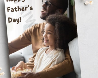 May include: A father and daughter are sitting on a couch, smiling and watching something. The daughter is holding a bowl of popcorn. The text "Happy Father's Day!" is written in brown letters on a white background.