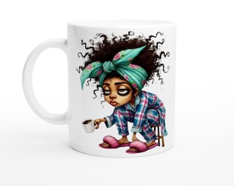 May include: White ceramic mug featuring a cartoon illustration of a sleepy person in pajamas holding a coffee cup. The character has curly hair, a teal headscarf, and pink slippers. The person is sitting on a small wooden stool.