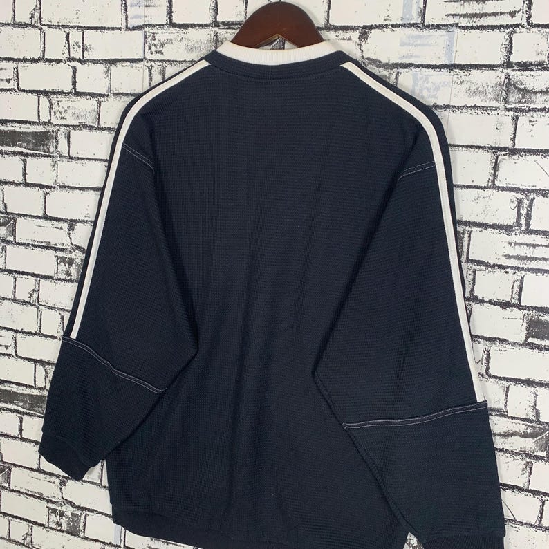 Puede incluir: Una camisa negra de manga larga con ribetes blancos alrededor del cuello y las mangas. La camisa tiene una textura acanalada.