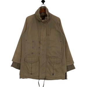 Puede incluir: Una chaqueta larga de manga larga de color marrón con cuello alto, cierre de cremallera y varios bolsillos. La chaqueta tiene un cordón de ajuste en la cintura y un cierre de botón en la parte delantera.