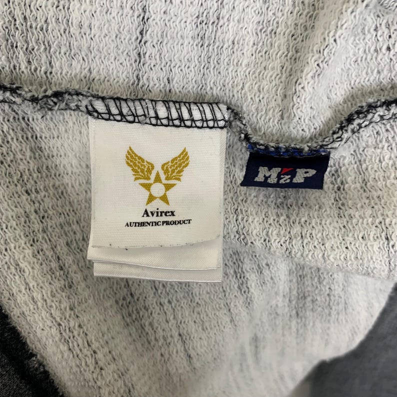 Puede incluir: Una sudadera con capucha a rayas blancas y negras con un parche de logotipo blanco y negro que dice "Avirex Authentic Product" y un parche de logotipo azul y blanco que dice "M.Z.P."
