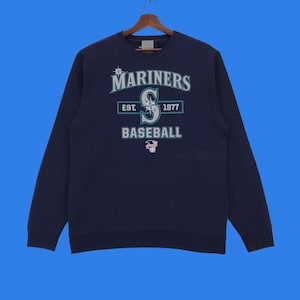 May include: A navy blue sweatshirt with the Seattle Mariners logo. The logo features the team's name, "Mariners", in white lettering with a green outline. The team's "S" logo is in green with a white star and a white outline. The text "EST. 1977" is in white lettering with a green outline. The text "BASEBALL" is in white lettering with a green outline.
