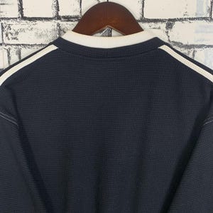 Puede incluir: Una camisa de manga larga de punto de gofre negro con ribetes blancos alrededor del cuello y los hombros.