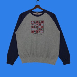 May include: A gray and navy blue sweatshirt with a red and white graphic of a word search puzzle. The puzzle says "ROAD, MOND, GET, THE, 1958, MATCHED GAME".