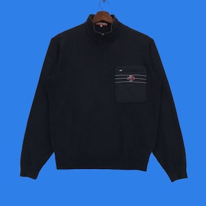 May include: A black long-sleeved sweater with a zippered collar and a black pocket on the left side. The pocket has a white and red logo with the text "Dickies" on it.