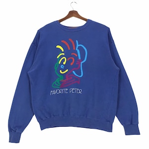 以下が含まれることがあります： 前面にカラフルな人物の顔のグラフィックと「FAVORITE PETER」の文字が書かれた青いスウェットシャツです。