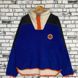 Puede incluir: Un jersey de polar azul, negro, blanco y naranja con cremallera. El jersey tiene un logotipo en la parte delantera que dice "Well-Pelle" con un círculo alrededor.