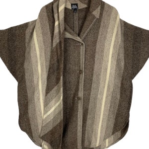 Könnte beinhalten: Ein braun-beiger Streifenponcho mit Kragen und drei Knopfverschlüssen. Der Poncho hat einen abgerundeten Saum und ein schalförmiges Panel mit vertikalen Streifen in Braun- und Beigetönen. Der Markenname "Park & Fifth" ist auf dem Etikett zu sehen.