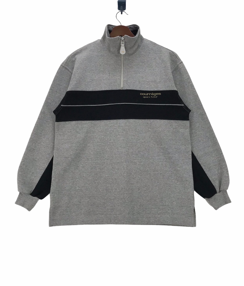 May include: A gray sweatshirt with black accents and a zipper. The sweatshirt has the text "Courr&egrave;ges Sport Future" on the front.