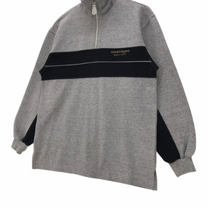 May include: A gray and black long-sleeve sweatshirt with a half-zip closure. The sweatshirt has a black stripe across the chest with the text "Courreges Sport Futur" in gold lettering.