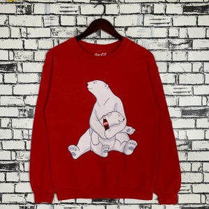 Puede incluir: Sudadera roja de Coca-Cola con un oso polar blanco y una cría que sostiene una botella de Coca-Cola. La sudadera tiene cuello redondo y mangas largas.