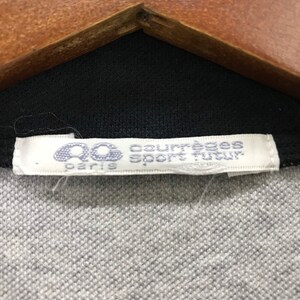 May include: A white tag with black text that reads "Courreges Sport Paris" on a black and gray shirt.