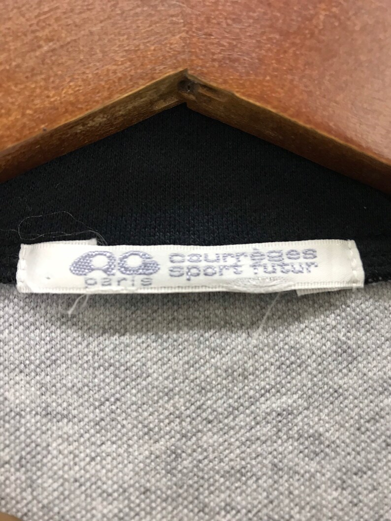 May include: A white tag with black text that reads "Courreges Sport Paris" on a black and gray shirt.