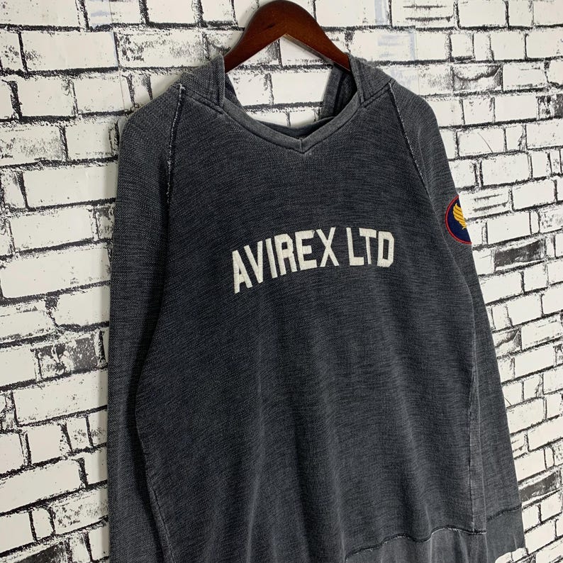 Puede incluir: Una sudadera con capucha negra con un aspecto desgastado. La sudadera tiene un logotipo bordado en blanco que dice "AVIREX LTD" y un peque&ntilde;o parche bordado en la manga.