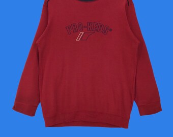 May include: Red sweatshirt with a black and navy blue trim around the neck and a navy blue embroidered logo that says "PRO-KEDS" with a stylized "K" that looks like a checkmark.