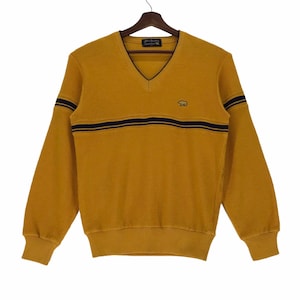 May include: A mustard yellow v-neck sweater with black stripes and a small embroidered bear logo. The sweater has long sleeves and a ribbed hem.